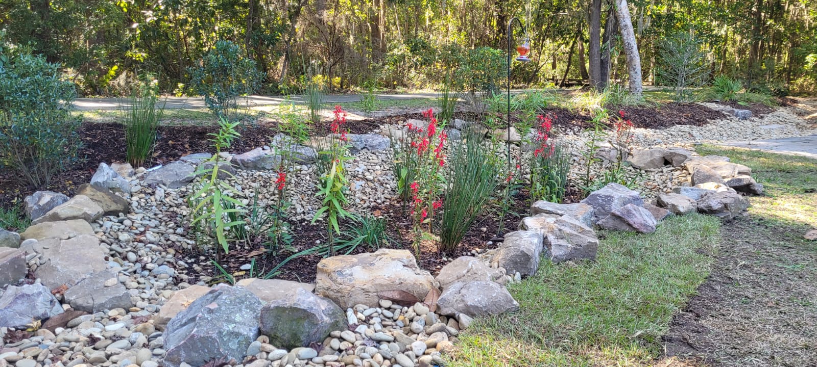 Blooming rain garden basin with red flowering perennials and native grasses framed by stone edging, designed by Victory Gardens in Savannah, GA