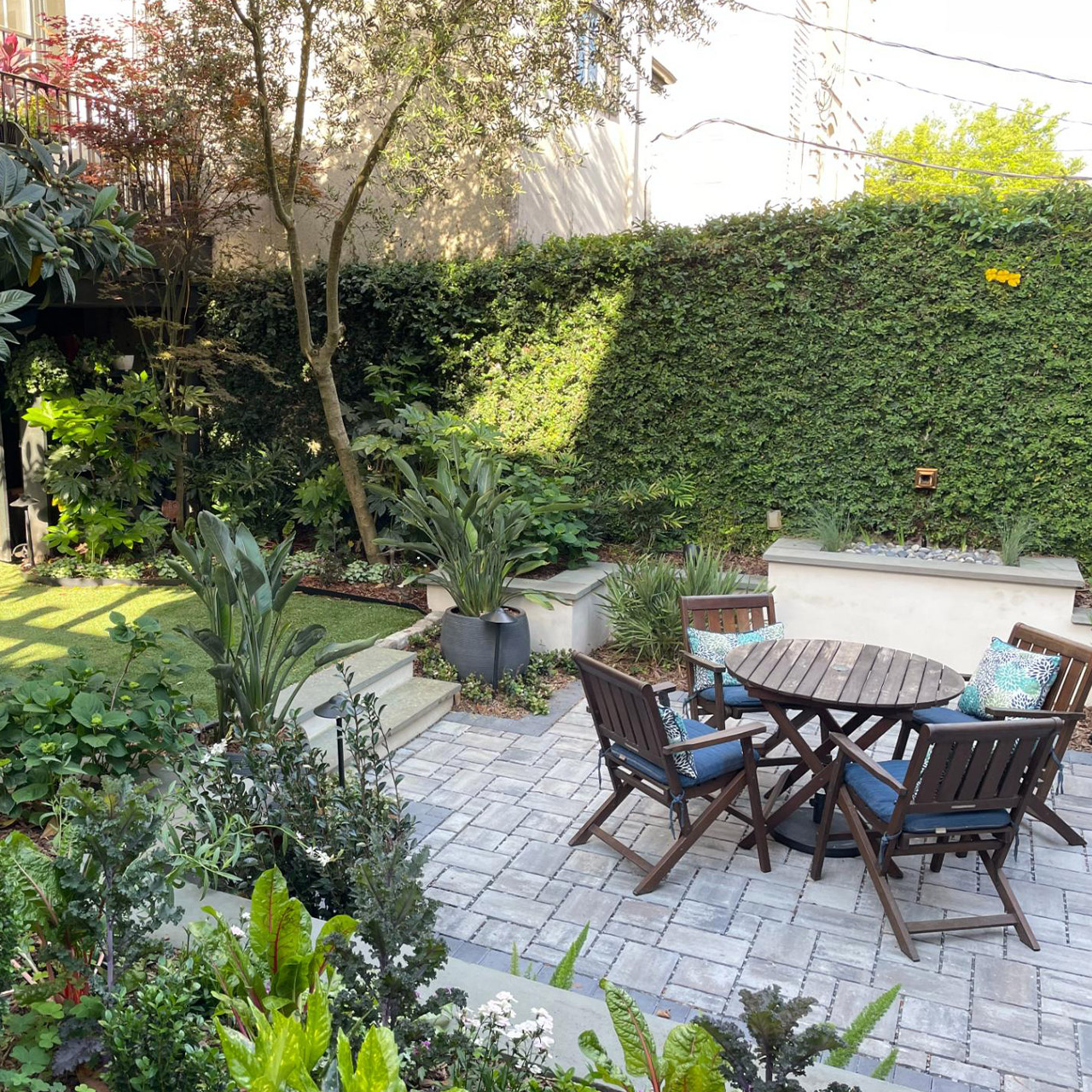 Courtyard with an ivy-covered wall and a small wooden table surrounded by chairs and greenery.